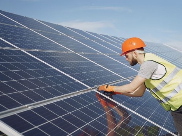 A man in an orange hat and vest working on solar panels.